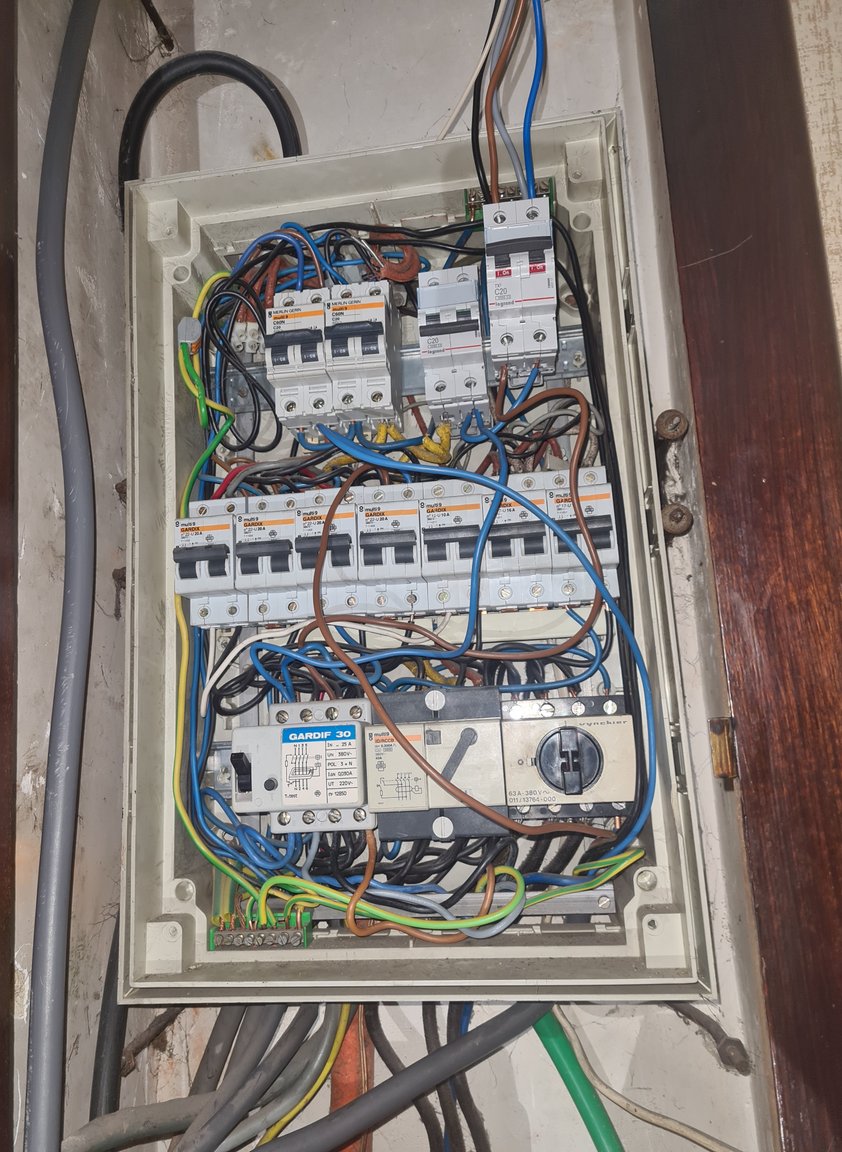 Oud verdeelbord in een houten kast met onoverzichtelijke bedrading, vóór de vernieuwing in Herent